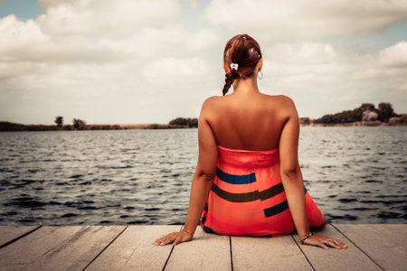 Rear view of woman relaxing on a pier while spending summer day at the beach.の写真素材