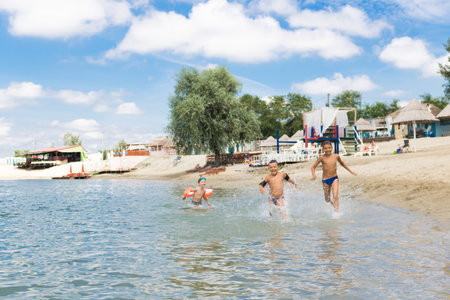 Small group of happy kids enjoying in summer vacation while running through water at the beach. Copy space.の写真素材