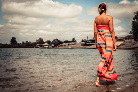 Rear view of carefree woman walking through the water at the beach.の写真素材