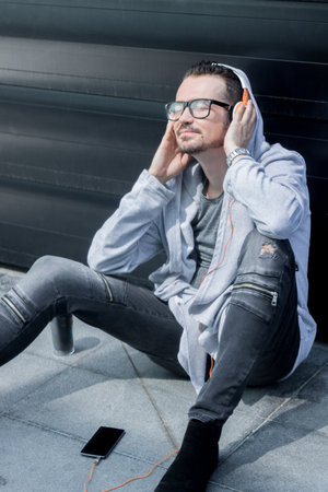 Smiling man listening music over headphones and relaxing outdoors with his eyes closed.の写真素材