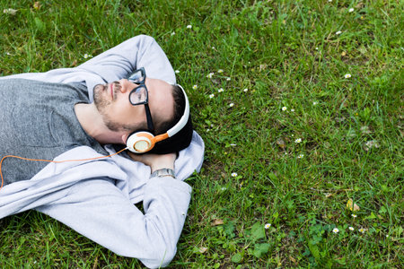 Carefree man listening music and daydreaming while relaxing on the field in spring grass.の写真素材