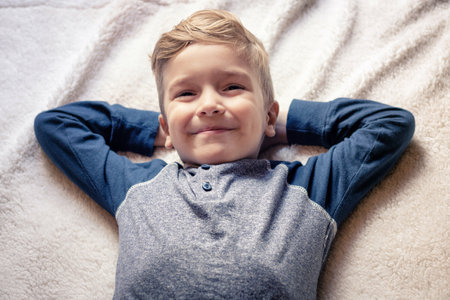 Happy kid with hands behind head lying on the bed and looking at camera.の写真素材