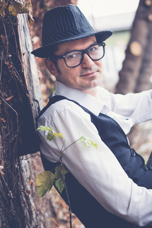 Portrait of smiling man wearing fedora hat and looking at camera while leaning on a wall outdoors.の写真素材