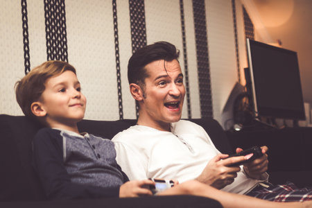 Excited father playing video games with his son and having fun at home.の写真素材