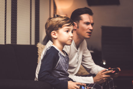 Small kid and his dad playing video game with wireless controllers at home.の写真素材