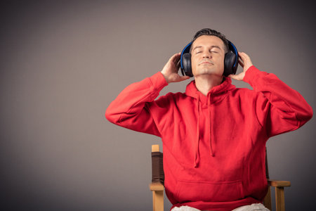Portrait of man listening music with eyes closed over the headphones against the wall. Copy space.の写真素材