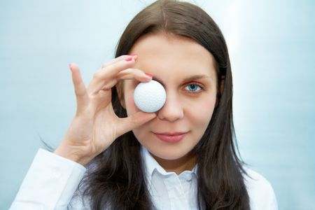 Young woman holding golf ball over eyeの写真素材