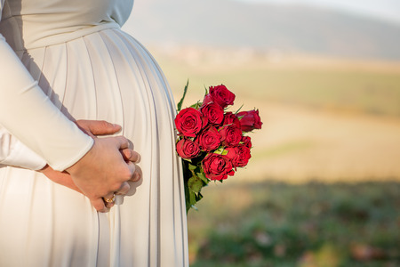 pregnant bride in white dress holding boquet of red rosesの写真素材
