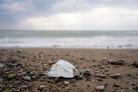 COVID-19 Mask on Stony Beach and Blurred Sea in Backgroundの写真素材