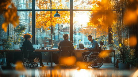 three people working at a desk by a large window with autumn trees and bright sunshine outside the glassの素材