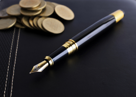 Fountain pen and coins stack on leather book for business finance conceptの写真素材