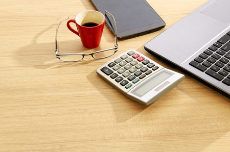 Calculator and eyeglasses with red cup coffee and tablet on wood table backgroundsの写真素材