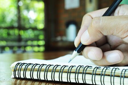 Right hand holding pencil for writting on notebook blank page with bokeh lights backgroundsの写真素材