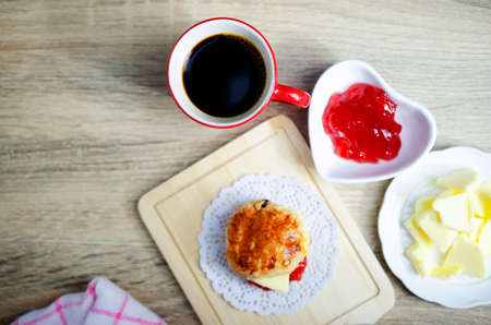 Close up of Red cup coffee drinks with scone and butter jam on wooden table backgrounds above, Top viewsの写真素材