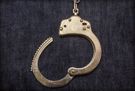 Police steel handcuffs lying on jeans backgroundの写真素材