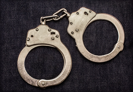 Police steel handcuffs lying on jeans background