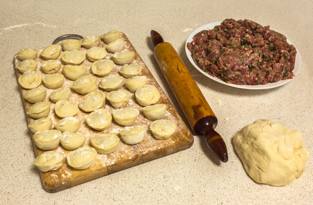 Fresh homemade ravioli on a wooden board, next to a plate of minced meat and dough with a rolling pinの写真素材