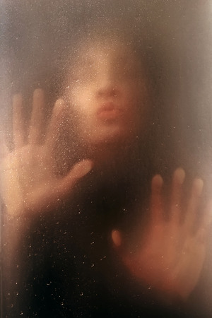 face and hands pretty girl on the wet glass with drops of rainの写真素材