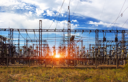 Electrical distribution station, transformers, high-voltage lines in sunrise with clouds