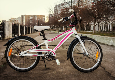 Women's bike in a retro-style, white with pink stripes on the background of urban architectureの写真素材