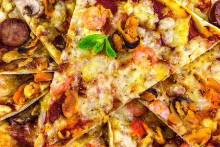 freshly baked pizza with salami, mussels and shrimp, fried pieces of close-up, garnished with fresh mintの写真素材