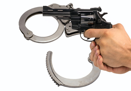 Gun in hand against the background of police handcuffs. Adventure and justice.