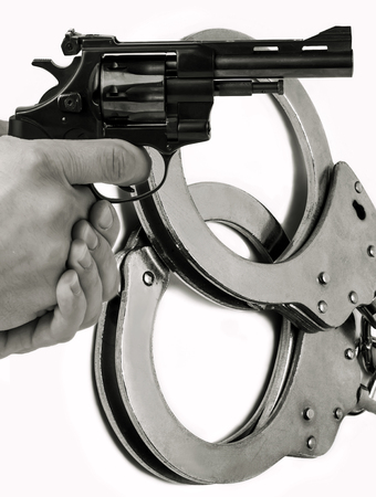 Gun in hand against the background of police handcuffs. Adventure and justice.の写真素材