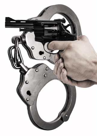 The gun in hand against the background of police handcuffs. Adventure and justice.の写真素材
