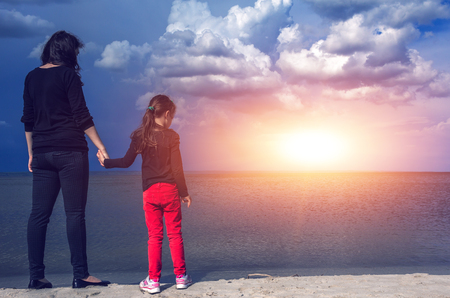 Young mother with her daughter on the beach at sunsetの写真素材