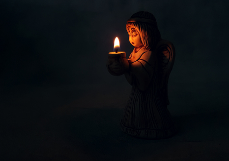 angel holds a burning candle in the dark. background religion, prayer and faith.の写真素材