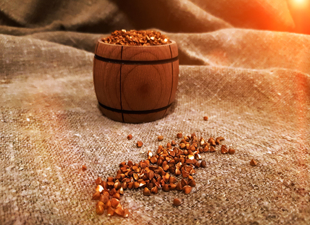 grains of buckwheat in a wooden barrel on burlap at sunset, rural background. Organic, diet food.の写真素材