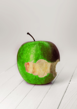 bitten green apple with dew drops on a white wooden background.の写真素材