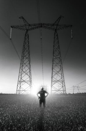 guy on the background of high-voltage power lines at sunset. green field. distribution station. high voltage electric transmission tower.の写真素材