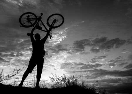 cyclist on the mountain with a bicycle, admiring the fiery sunset.の写真素材