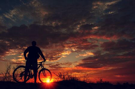 cyclist on the mountain with a bicycle, admiring the fiery sunset.の写真素材