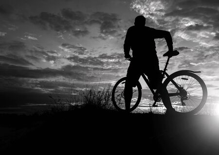 cyclist on the mountain with a bicycle, admiring the fiery sunset.の写真素材
