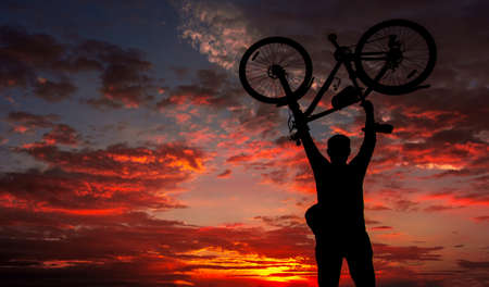 tourist with a bicycle on the background of a fantastic fiery sunset. cyclist silhouette.の写真素材