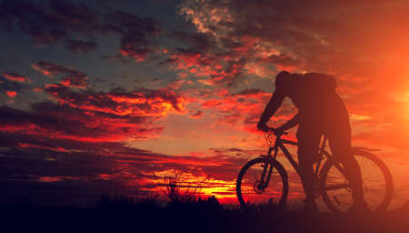 cyclist on the mountain with a bicycle, admiring the fiery sunset.の写真素材