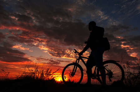 cyclist on the mountain with a bicycle, admiring the fiery sunset.の写真素材