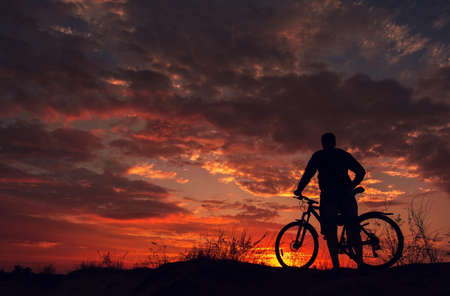 cyclist on the mountain with a bicycle, admiring the fiery sunset.の写真素材