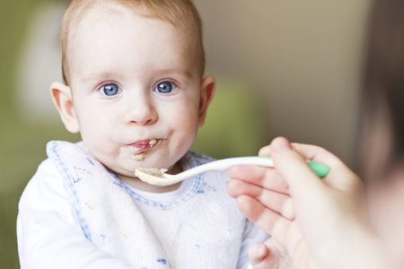 Hungry baby boy with blue eyes eating porridgeの写真素材