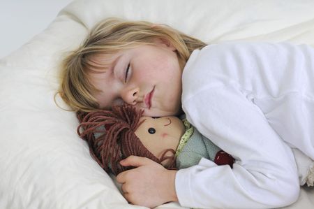 Blond little girl with puppet sleeps in bedの写真素材