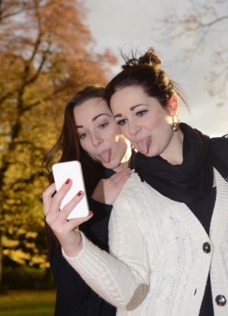 cheeky girlfriends with smartphone in autumn parkの写真素材