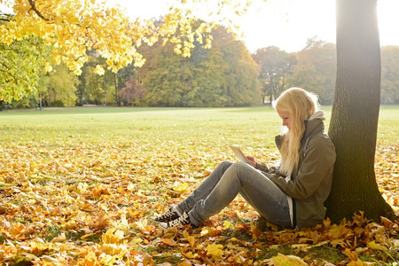 young woman with digital tablet in autumn parkの写真素材