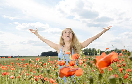 happy young blond woman cheering in poppy fieldの写真素材