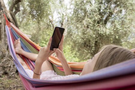 young girl with smartphone lying in hammockの写真素材