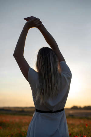 happy young blond woman enjoying sunset in poppy fieldの写真素材