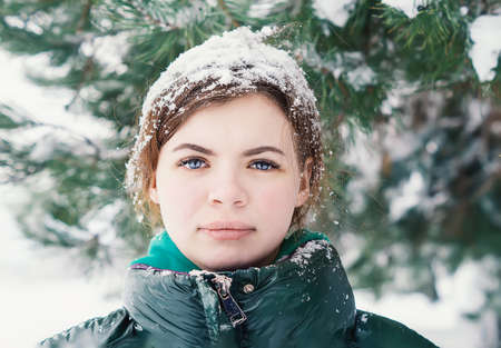 Beautiful young woman on a snowy winter day with snow flakes on her hair. A teenage girl under a...