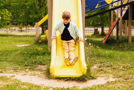 A pretty little girl goes down the slide on the playground. In Summer, A Carefree 4-5-Year-Old Girl Rides A Plastic Children's Slide On The Playground. Children's outdoor games. healthy lifestyle.の写真素材
