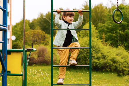 A playful little baby girl climbed an iron ladder on an outdoor playground on a sunny day. A...
